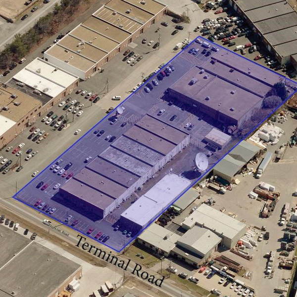 Aerial view of industrial buildings outlined in blue along Terminal Road, surrounded by parked cars and adjacent warehouses. The outlined area highlights a specific property within a larger industrial complex.